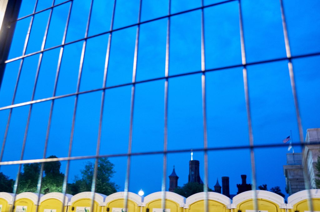 Smithsonian buildings seen through metal fencing above portable toilets