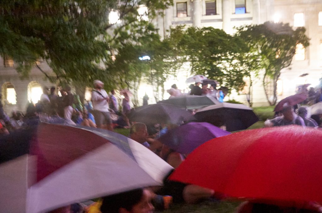 Attendees under umbrellas beneath trees at night