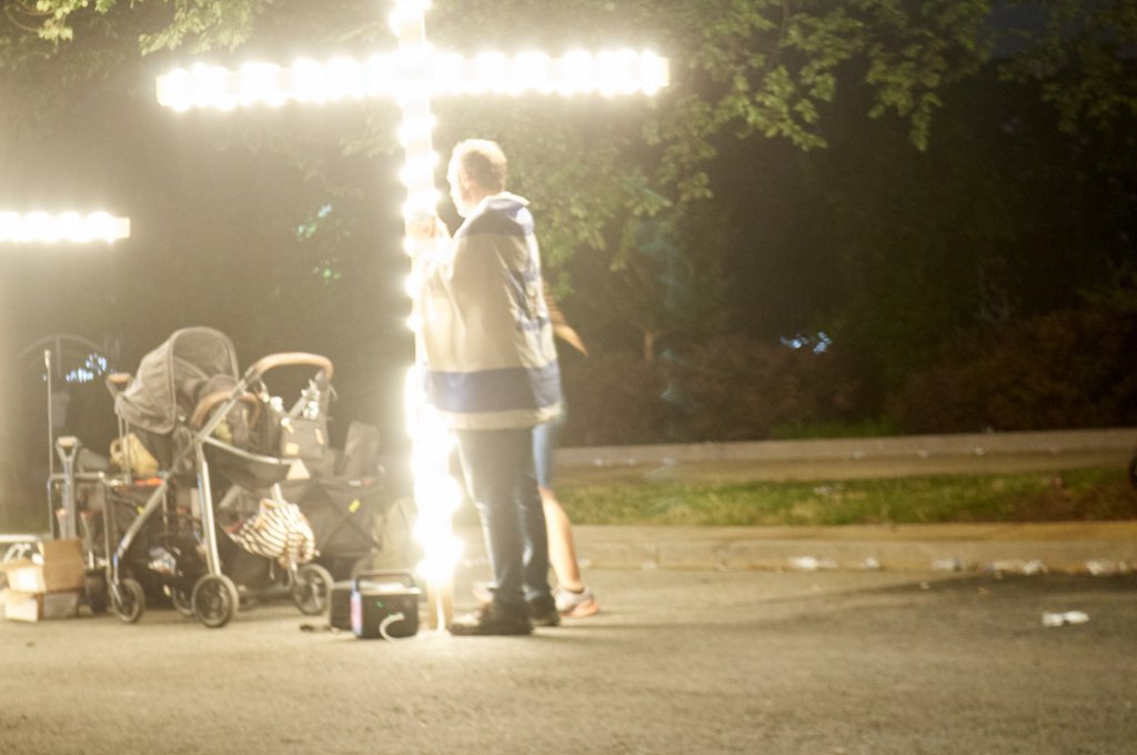 Man beside an illuminated cross and a stroller at night