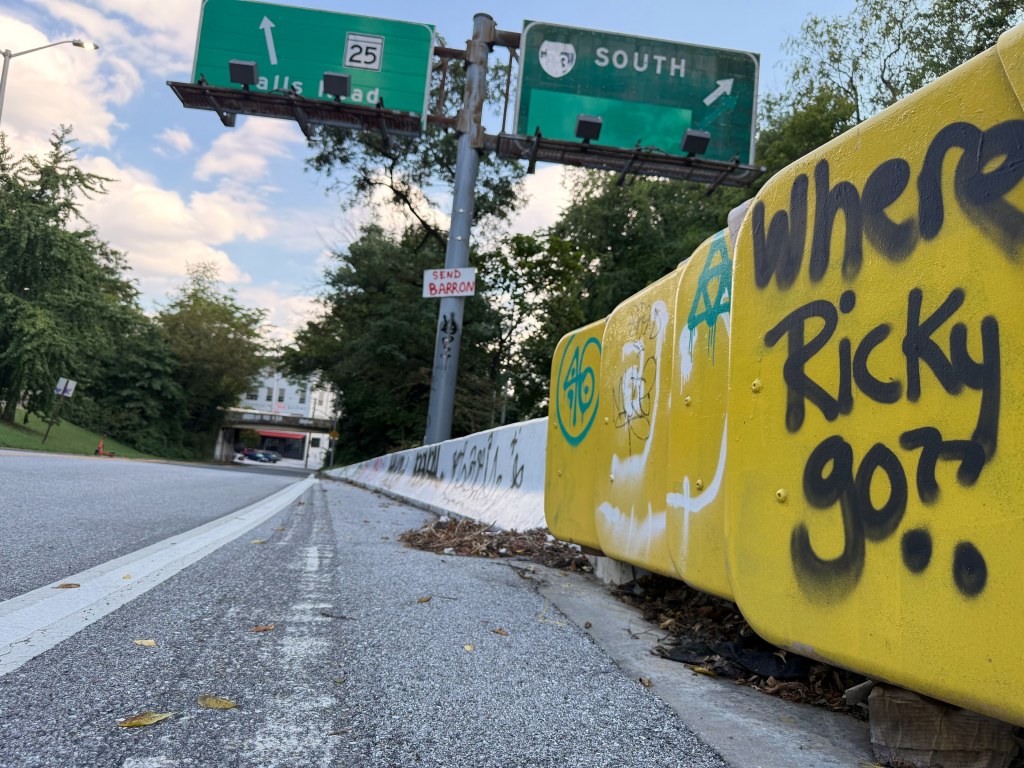Yellow barrier painted Where Ricky go? with overhead signs beyond