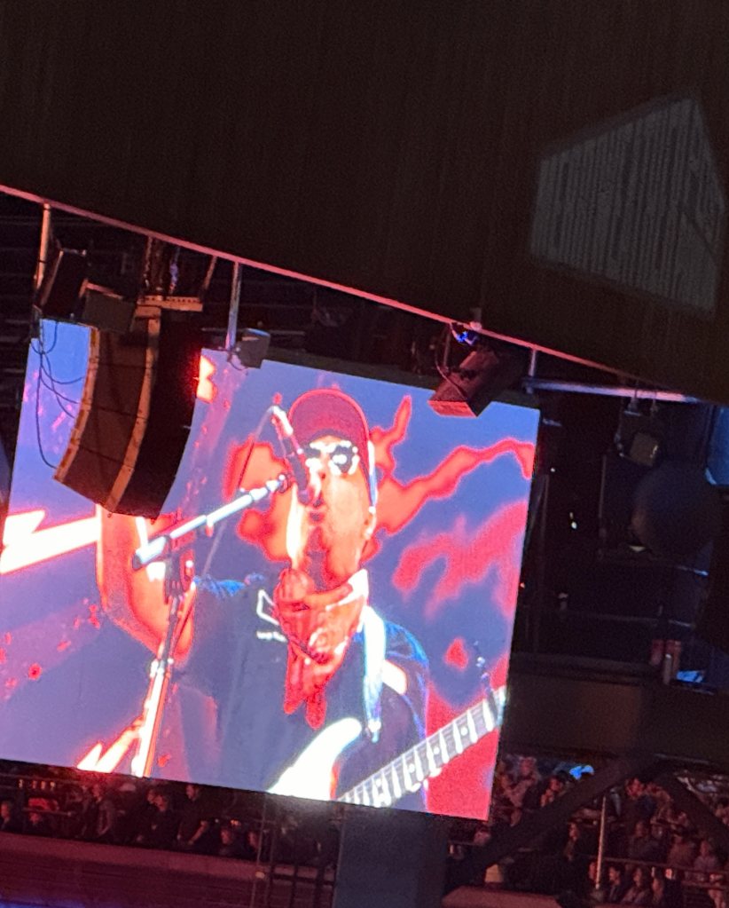 Tom Morello performing on video screens beside the stage