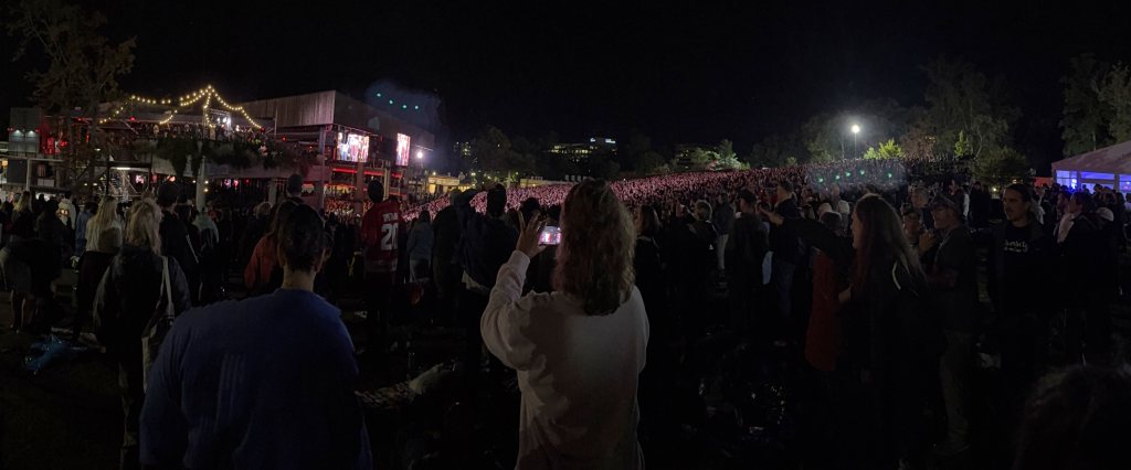 Panorama of the crowd on the lawn at night, a woman recording on her phone