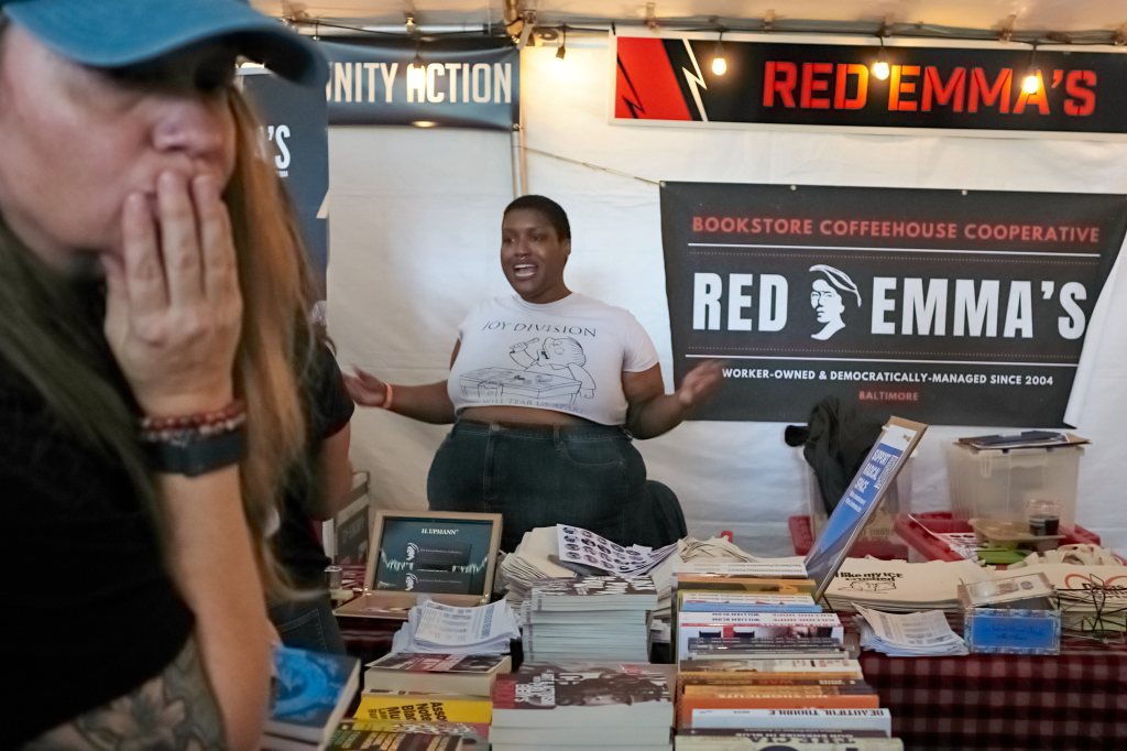 Worker talking with festivalgoers at a book table under a Red Emma’s banner